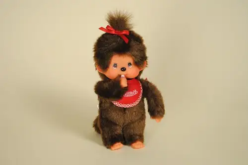 Peluche Monchhichi avec bavoir et nœud rouge mesurant 20 cm de haut de la marque Sekiguchi