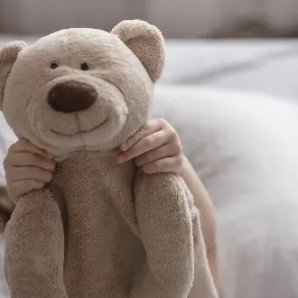 Enfant tenant un ours en peluche beige dans une chambre, symbole du lien affectif avec un doudou